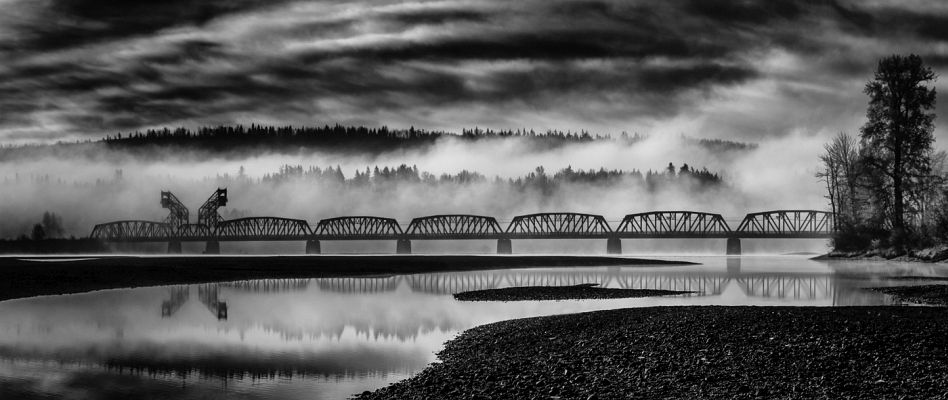 A monochrome image of a train bridge over a river